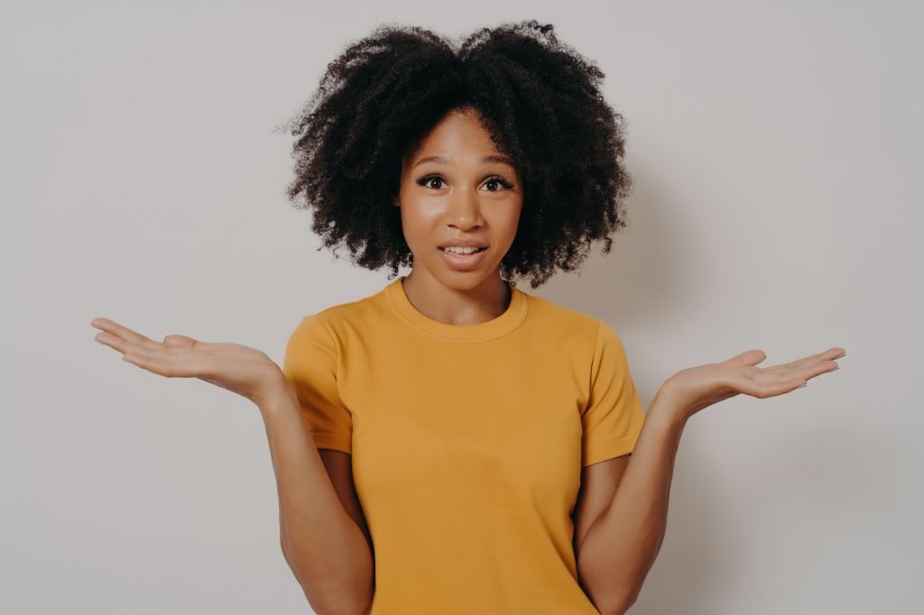 Confused doubtful black woman shrugging with shoulders, feeling baffled while looking at camera